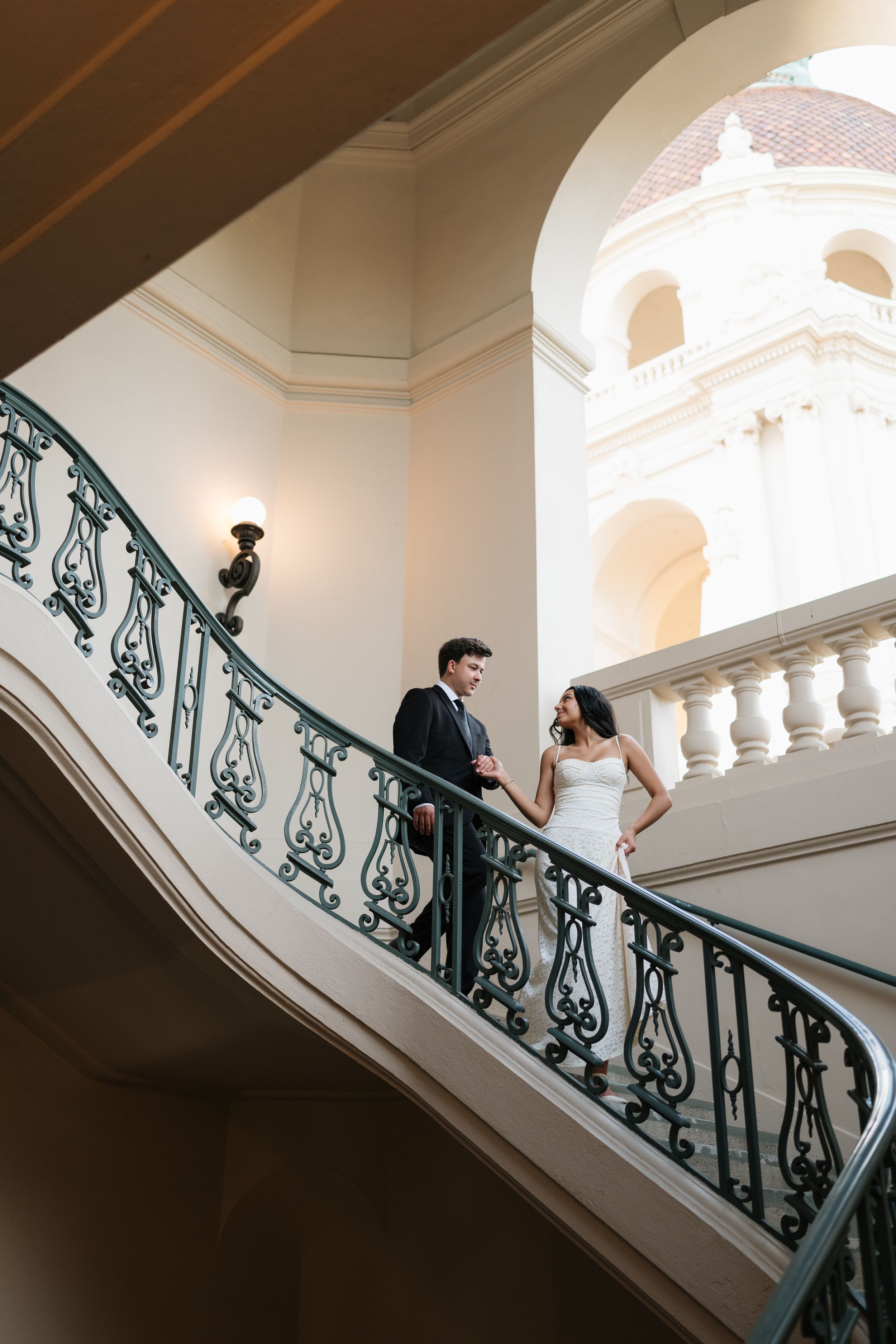 Couple holding hands on elegant curved staircase. Fresno California Wedding Photographer and Videographer