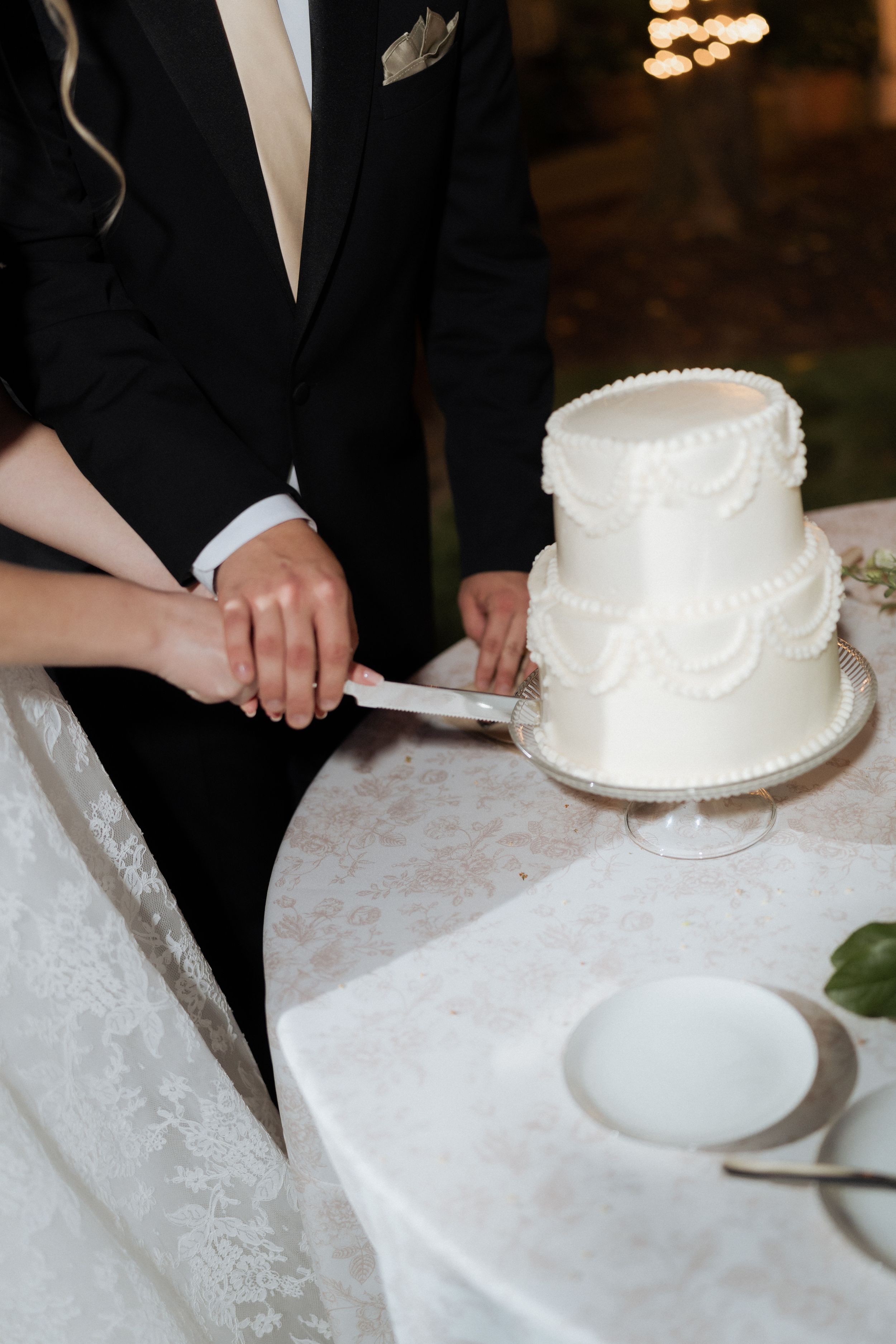 Bride and groom cutting two-tier white wedding cake with pearl piping detail at reception. Fresno California Wedding Photographer and Video