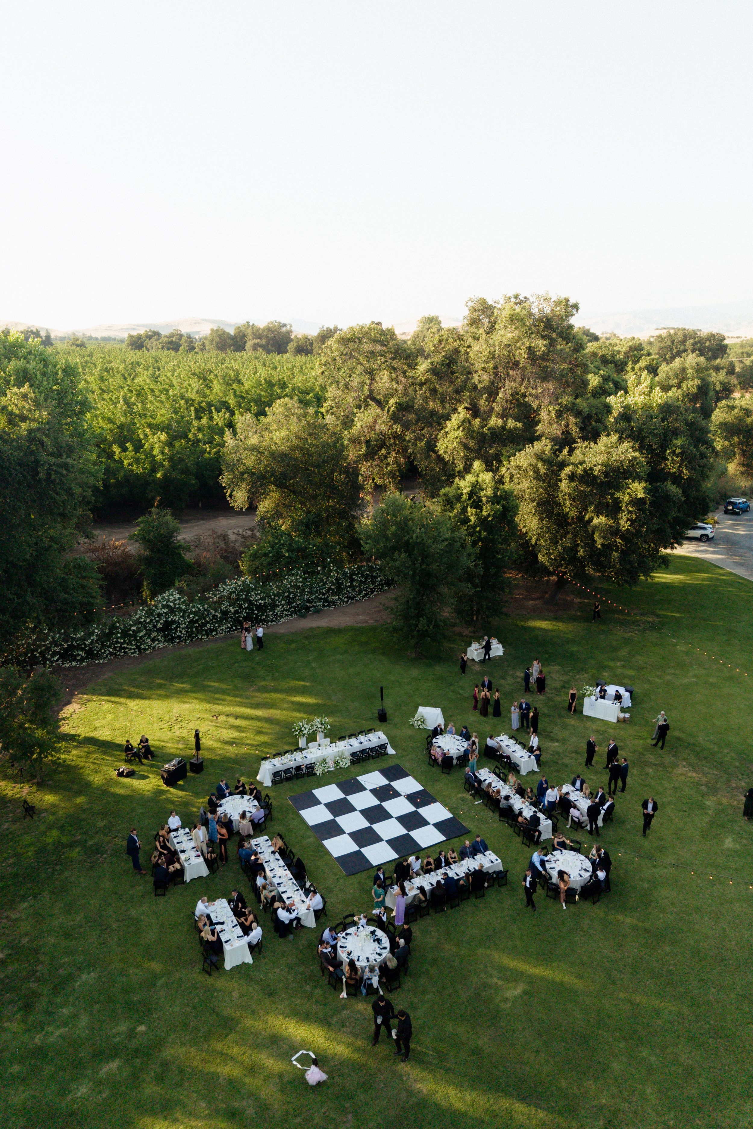 Aerial view of an elegant outdoor wedding reception with a giant chess board dance floor on a green lawn. Fresno California Wedding