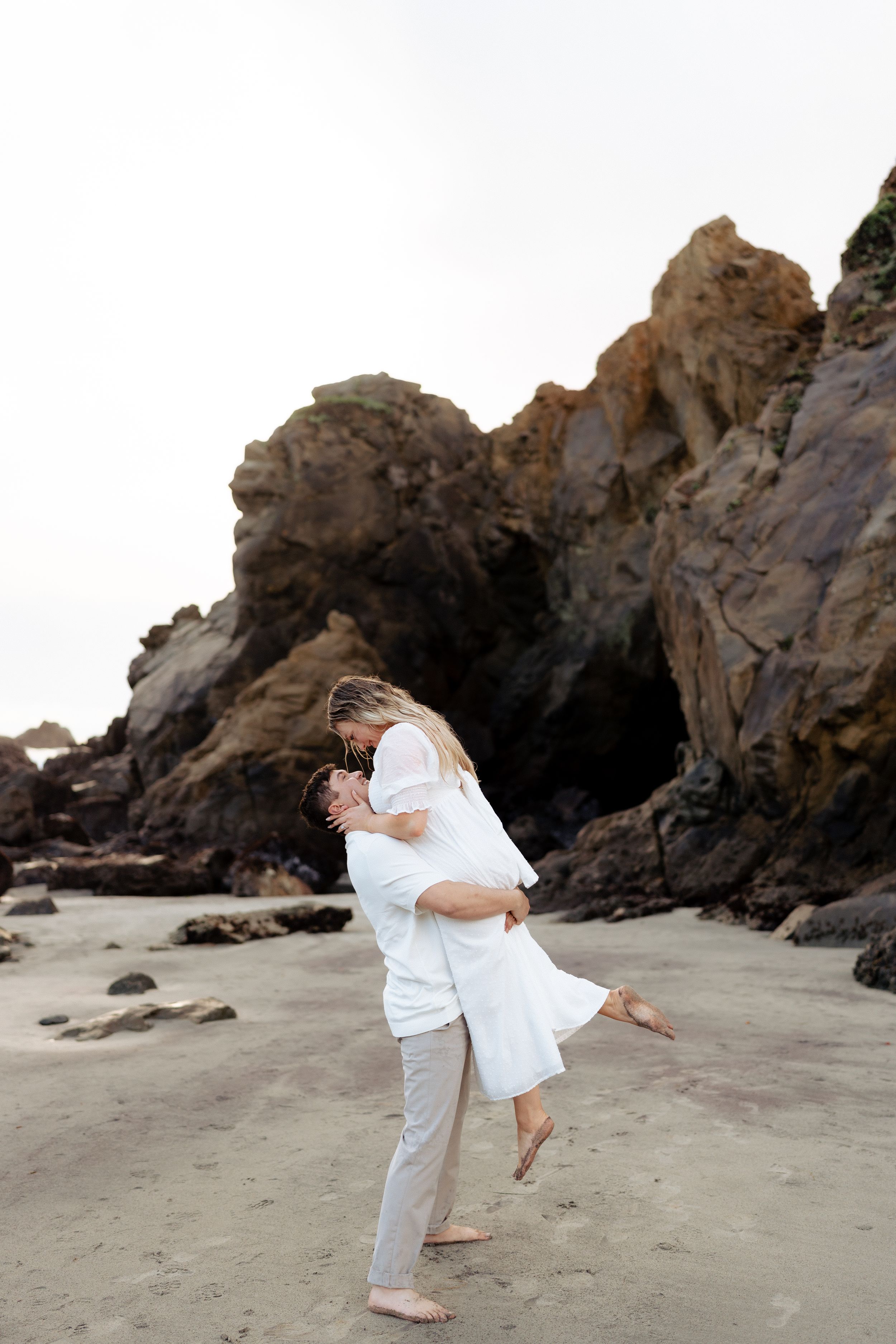 Couple embracing on a sandy beach with rocky cliffs. Fresno California Wedding Photographer and Videographer
