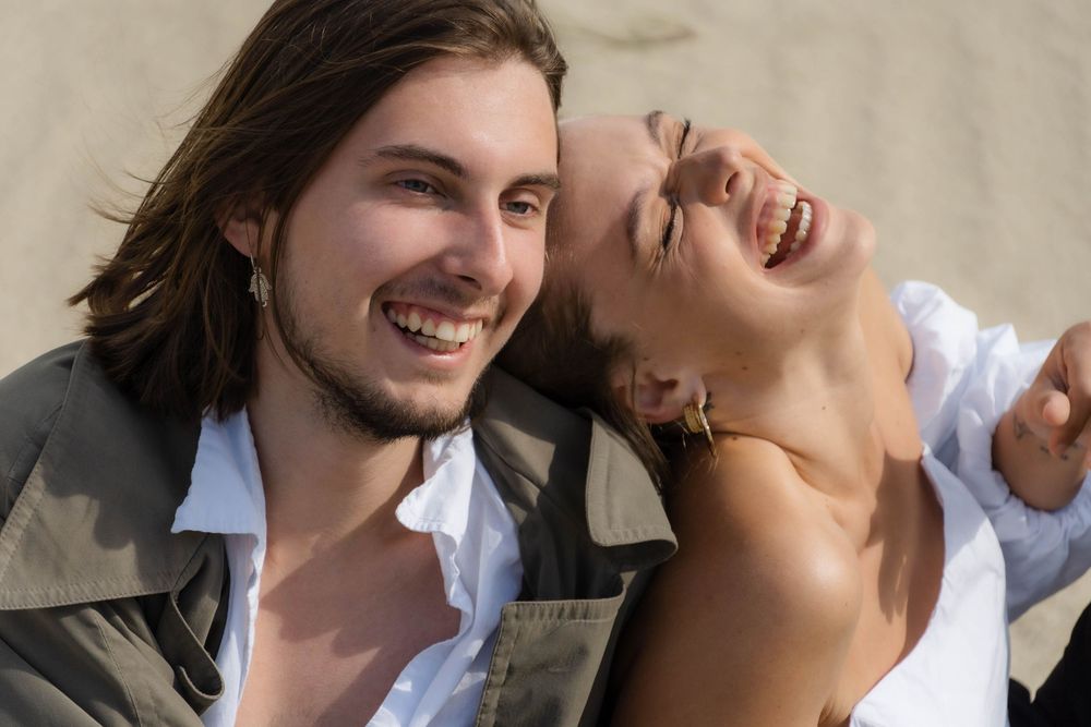 A woman is leaning on the man at the seaside and laughing together.