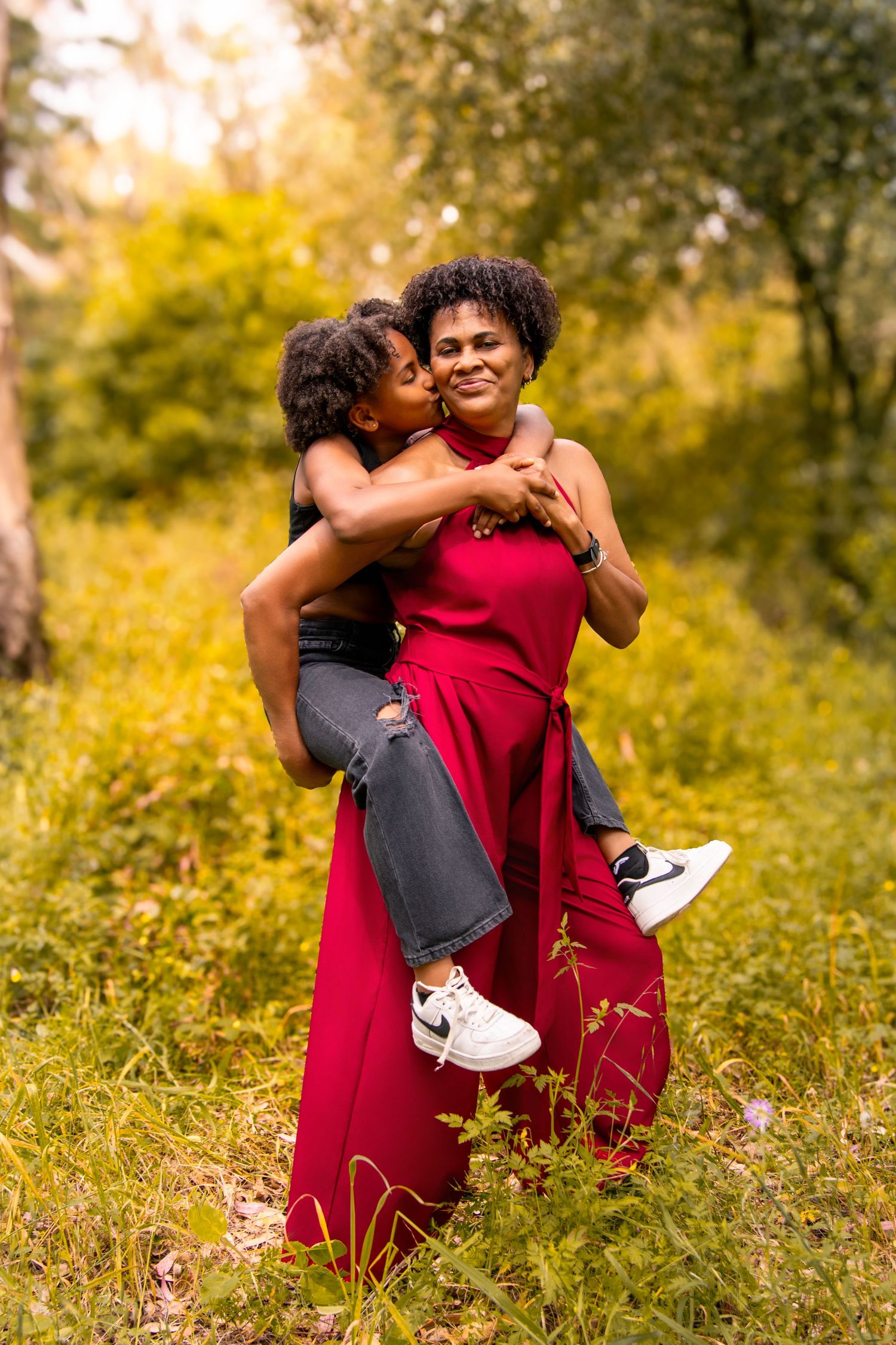 A joyful embrace captured in a golden meadow with natural sunlight filtering through the trees.