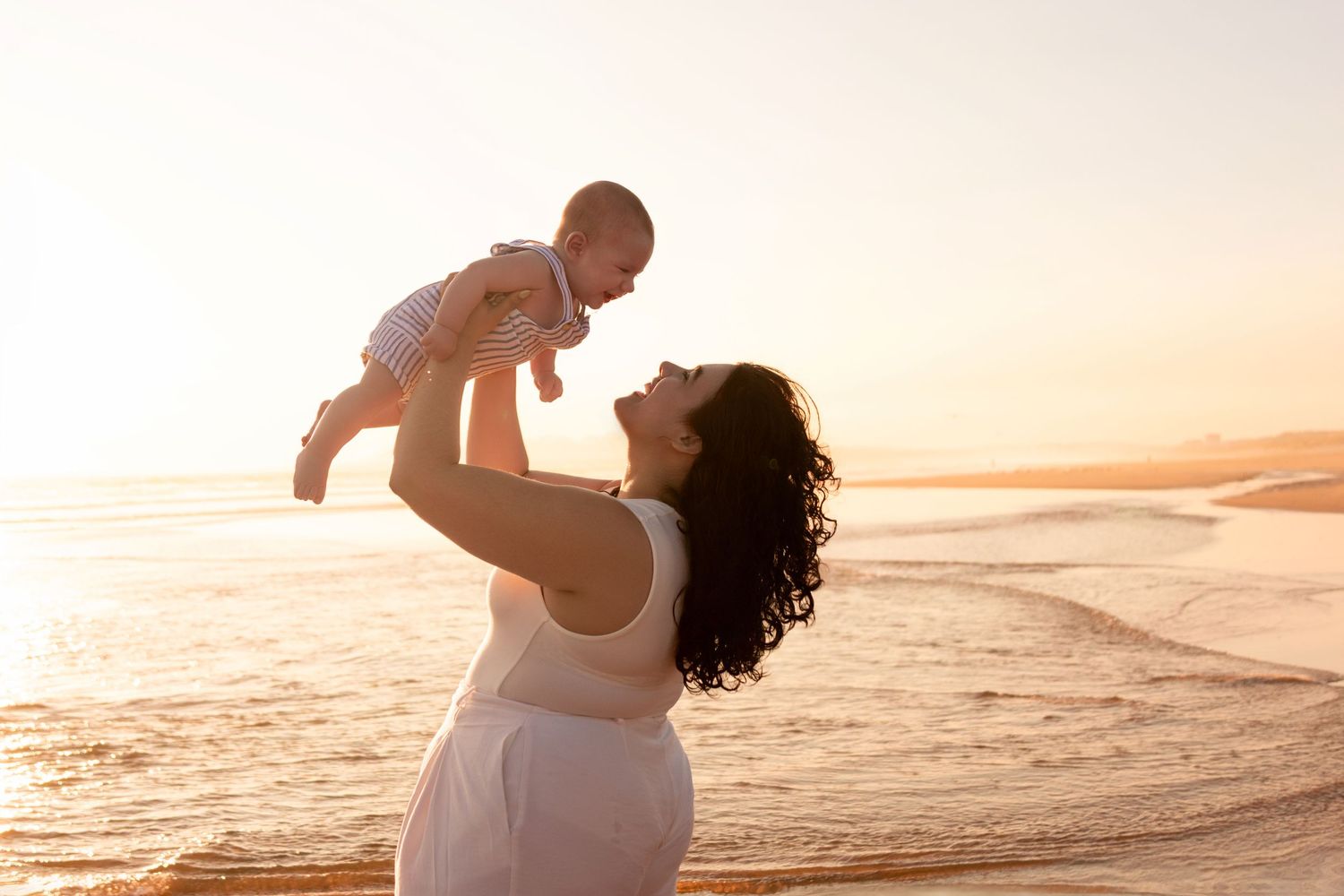 A tender moment between parent and baby during golden hour sunset at the beach.