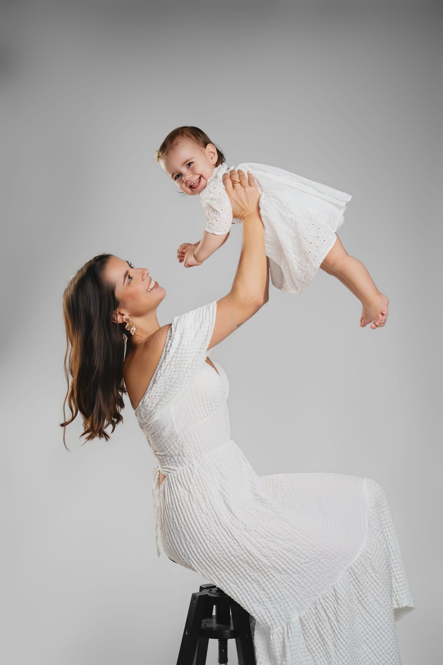 Artistic portrait in white dress against grey background showing playful movement and interaction.