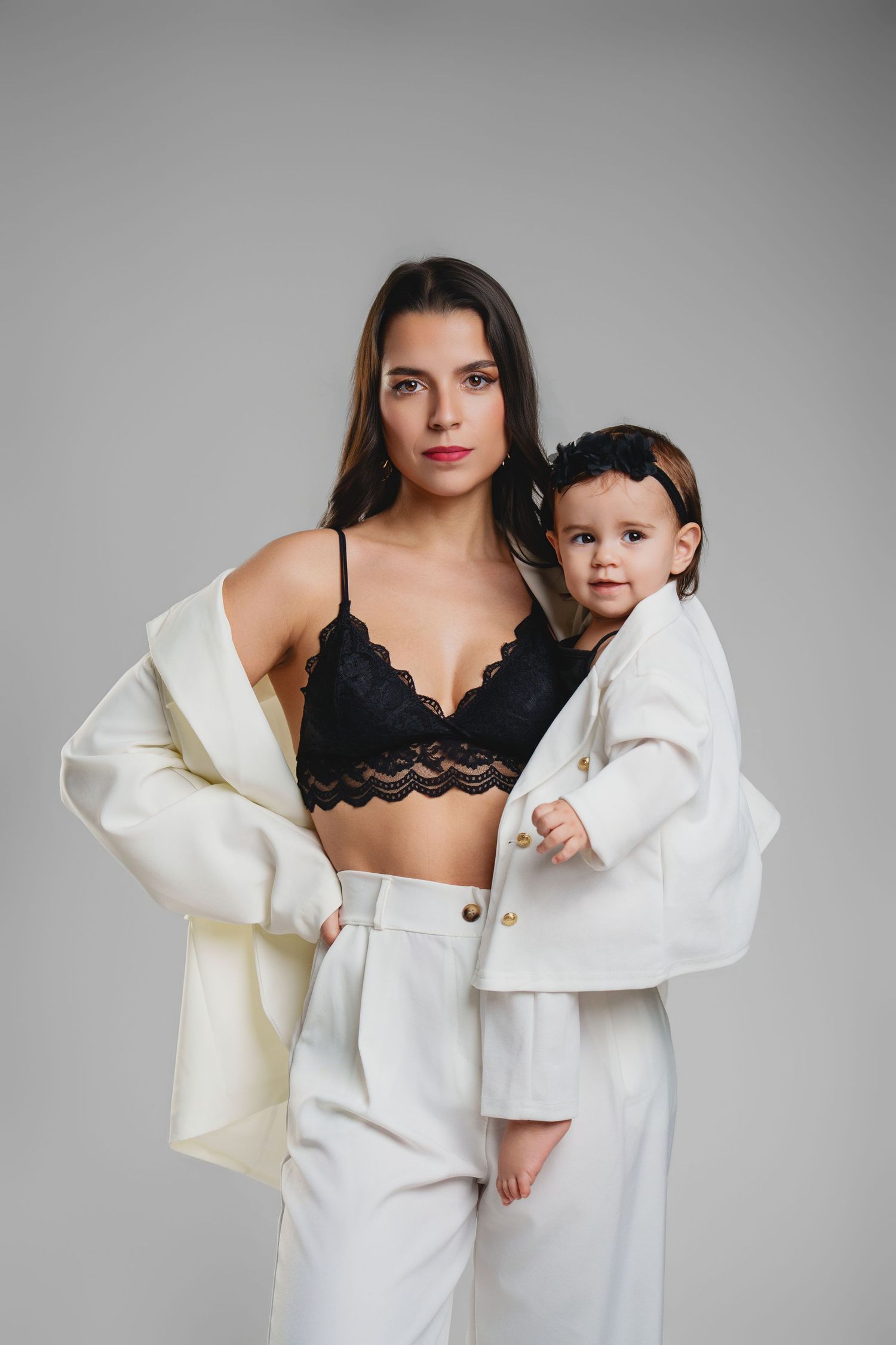 Modern portrait featuring white blazer and black lace bralette against grey studio backdrop.