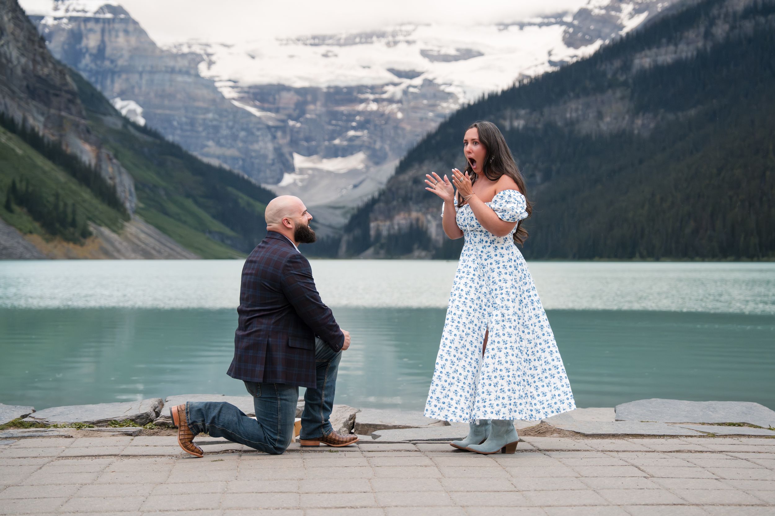 A couple poses together in front of Lake Louise with majestic snow-capped mountains in the background.