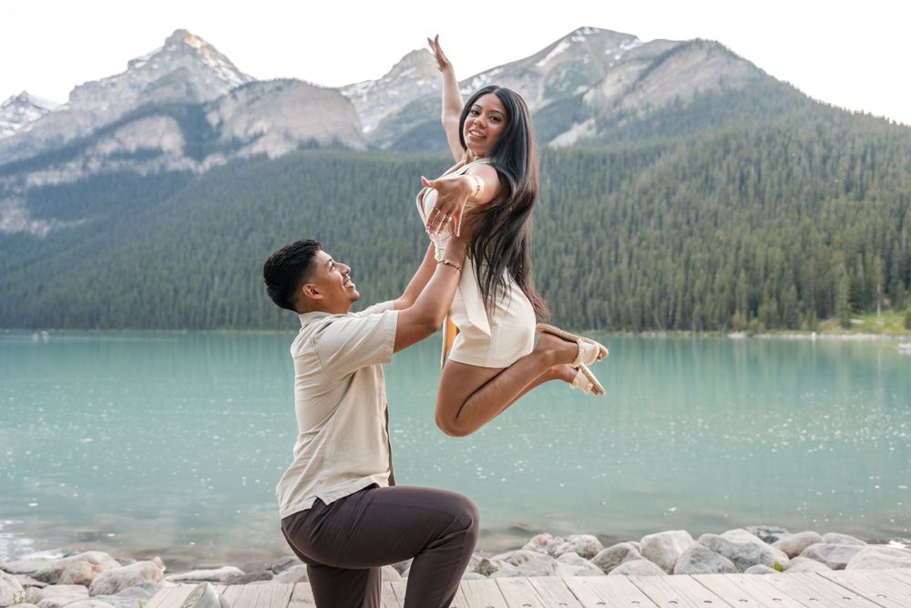 Woman jumps in air showing off engagment ring as fiance looks up at her