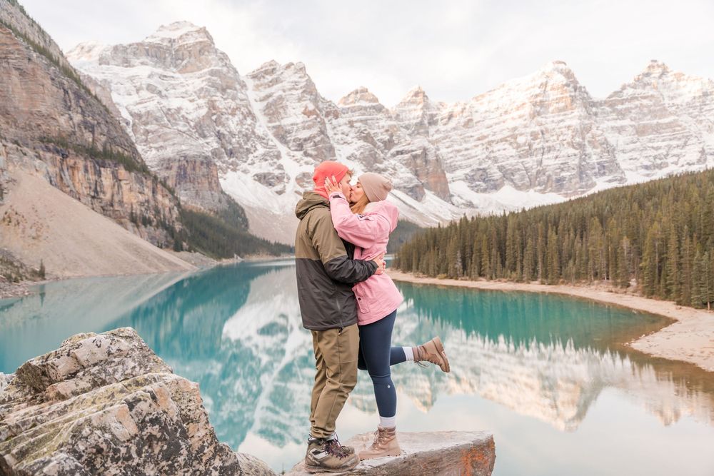 Couple embracing at Moraine Lake, Banff, with turquoise water and snow-capped Rocky Mountains reflected in the background.