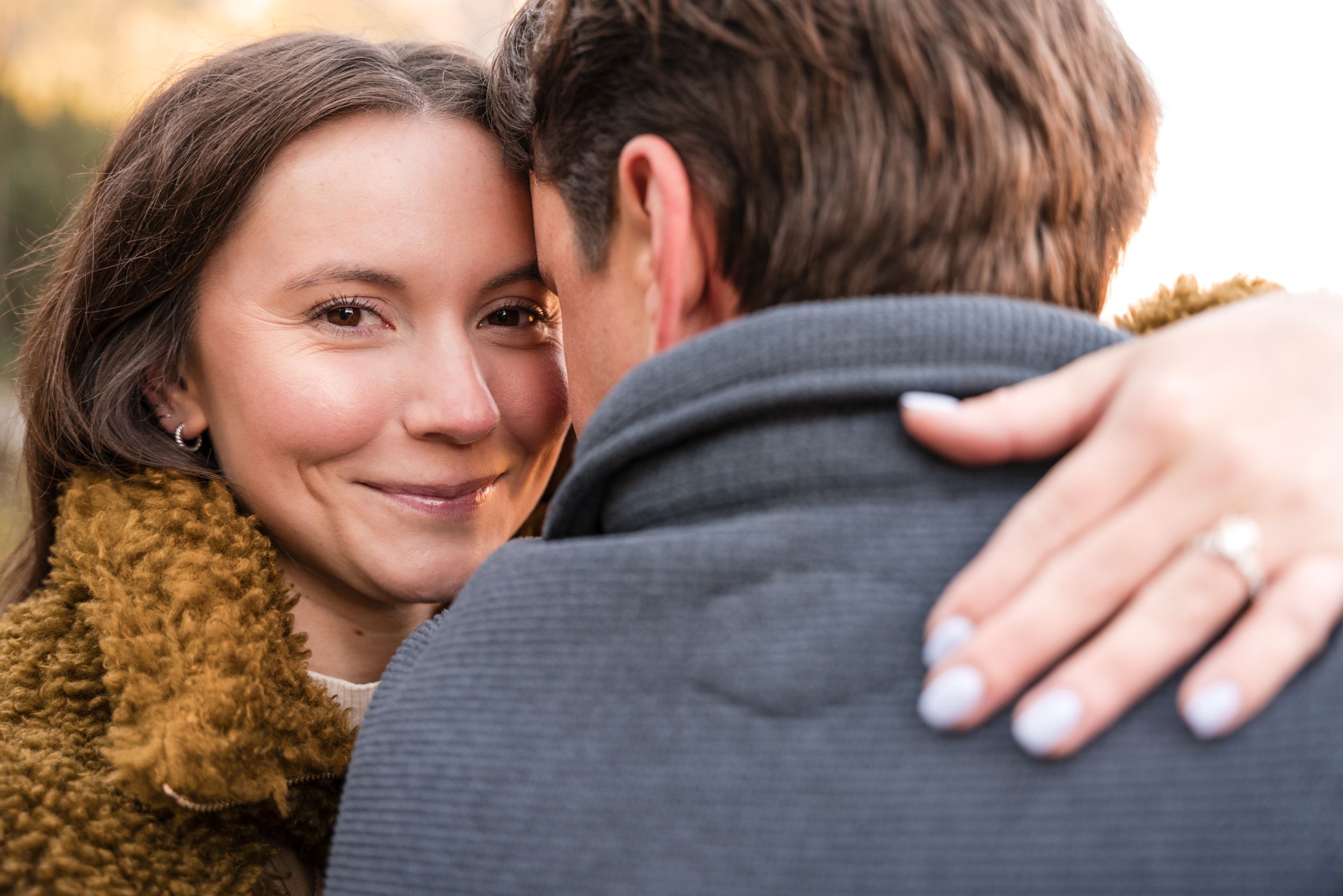 A tender embrace between a couple outdoors with a mustard yellow scarf visible in the frame.