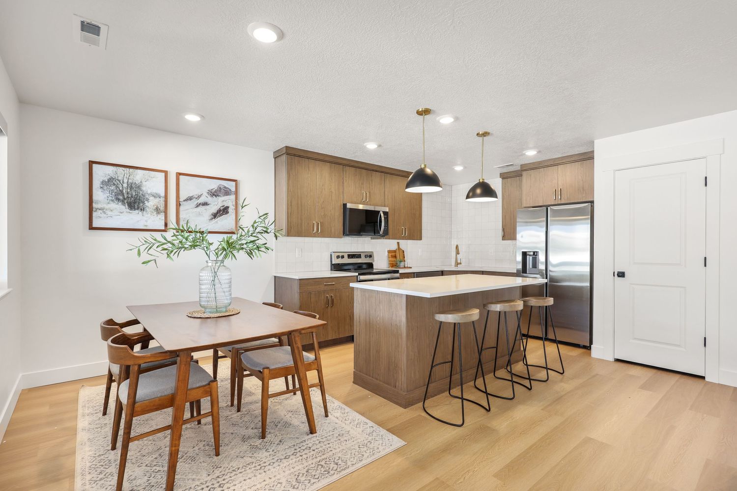 Modern kitchen with wood cabinets, island with seating, pendant lights, and light hardwood floors. Captured by Slate Media (best in UT)