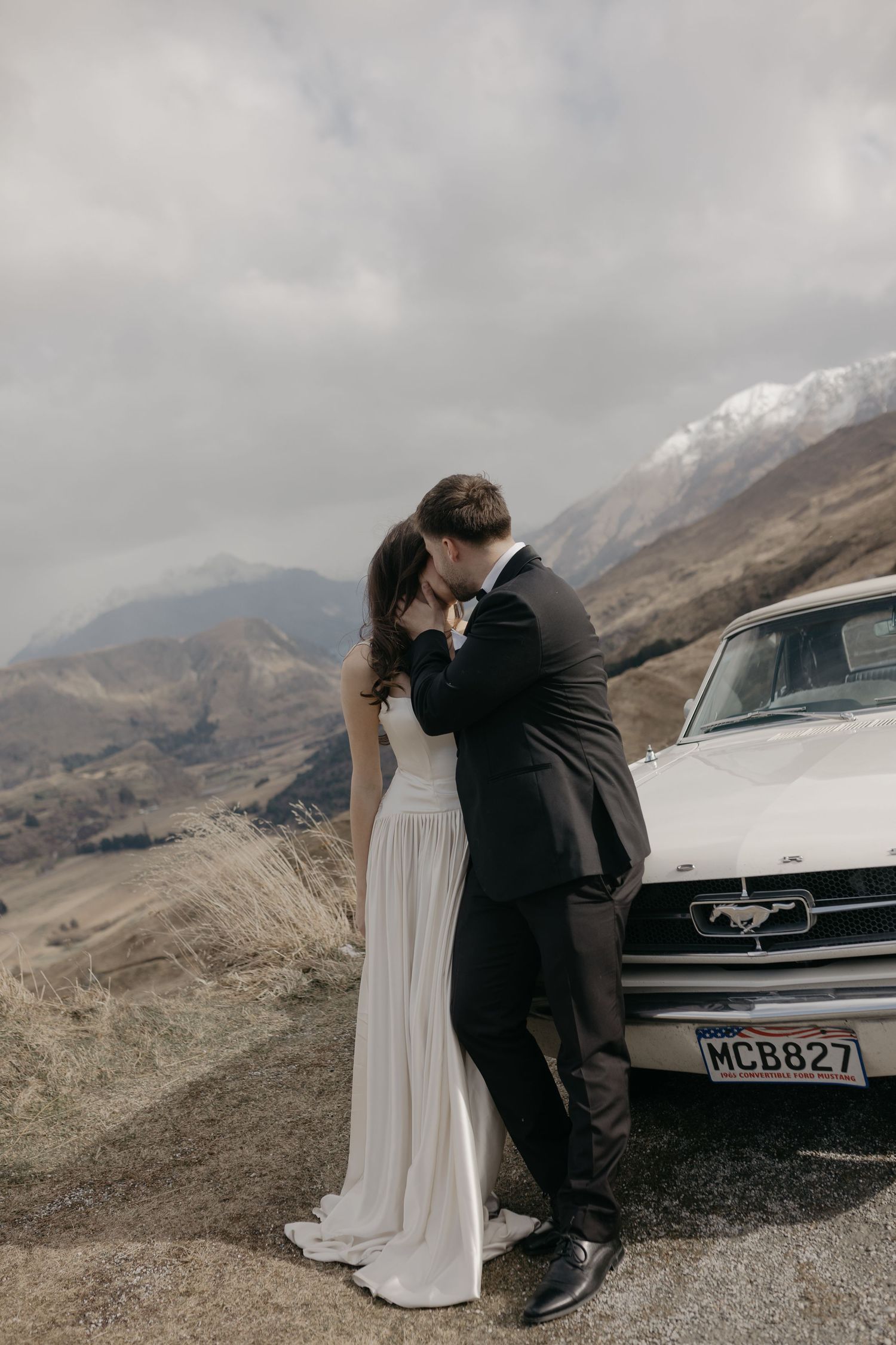 Elegant black and white portrait of a bride and groom sitting in a vintage car on their wedding day.