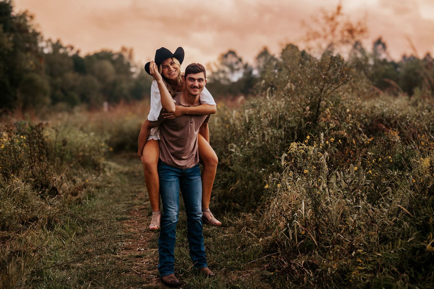 Romantic couple embracing in field during dramatic sunset sky.