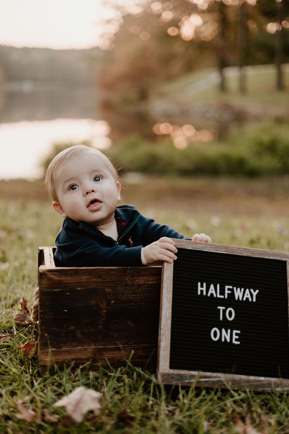 Outdoor sunset photo with wooden box and 'Halfway to One' letter board sign.