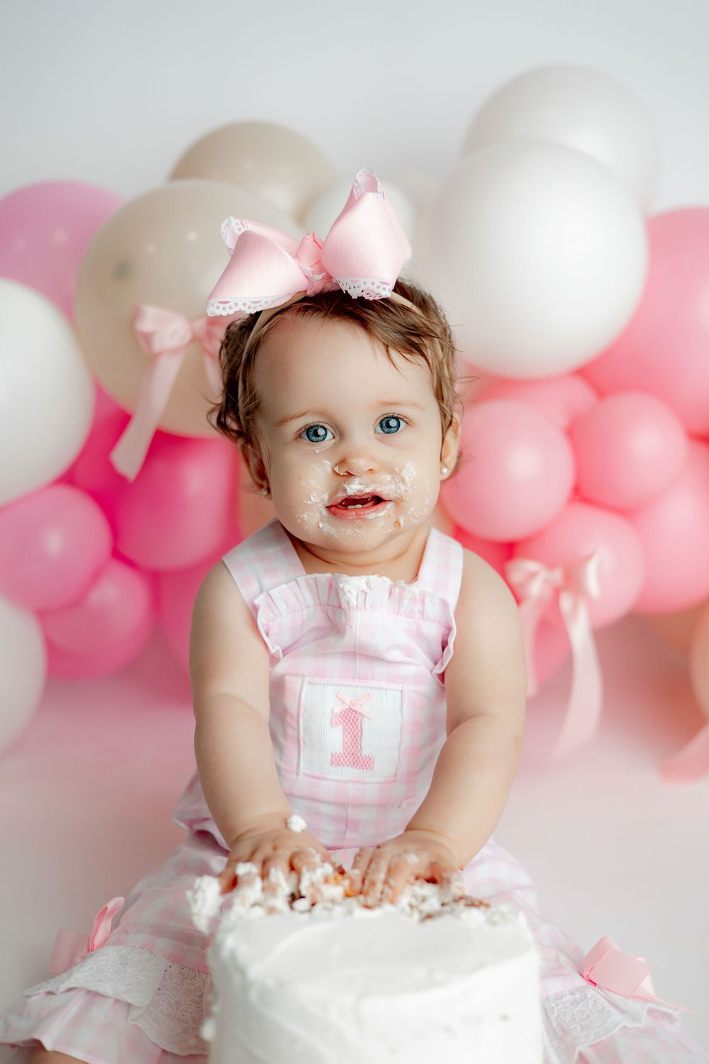 Birthday cake smash photoshoot with pink and white balloon backdrop and decorative number one.