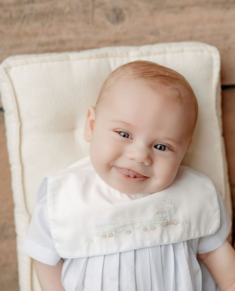 Studio portrait on cream cushion wearing white embroidered outfit.