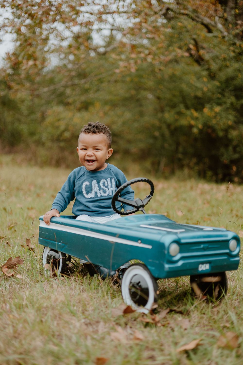 A joyful moment with a vintage-style blue pedal car against an autumn backdrop.