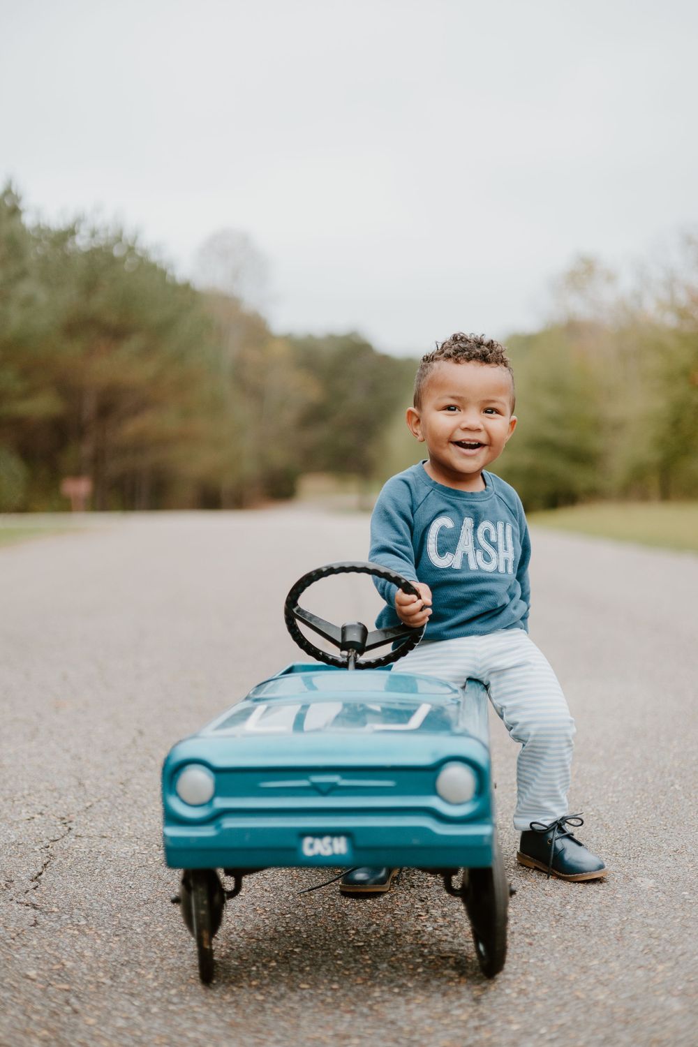 A teal-colored vintage pedal car being enjoyed on a peaceful road.