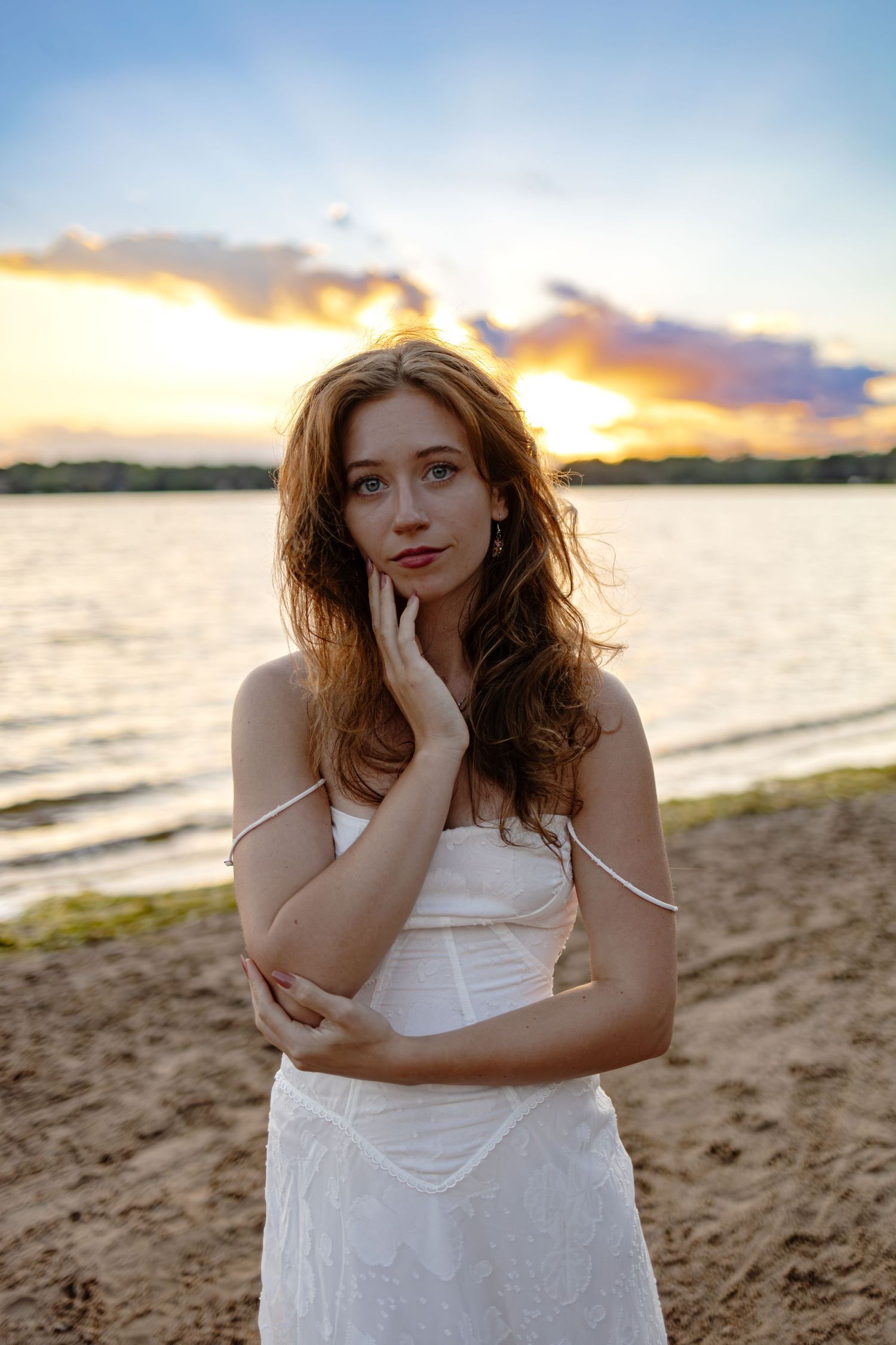 Sunset portrait of a woman in a white dress standing on a beach.