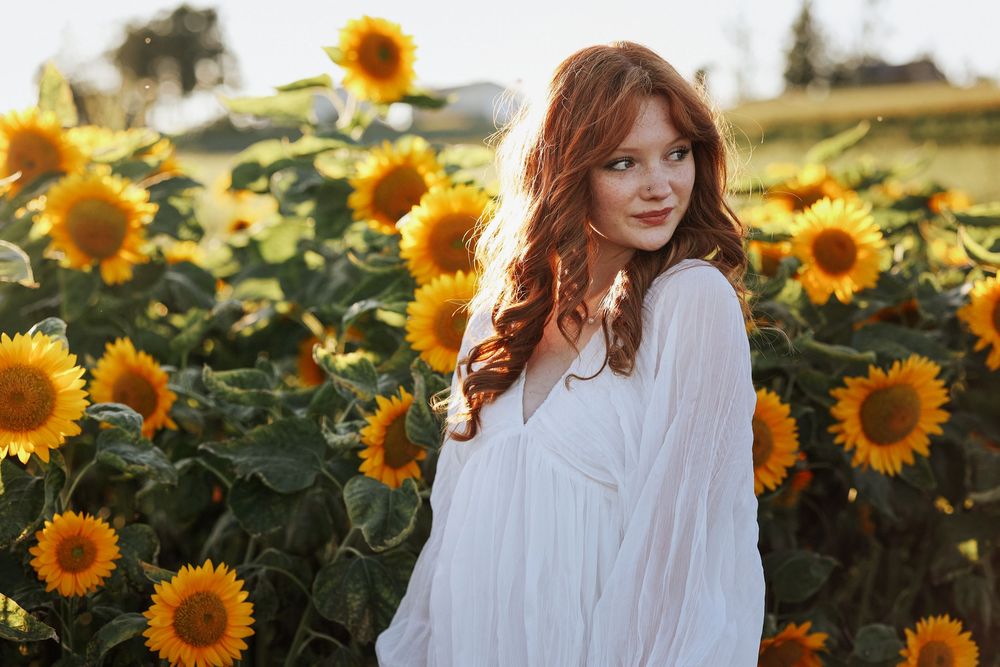 Ethereal portrait in a sunflower field at golden hour featuring white dress and flowing hair.