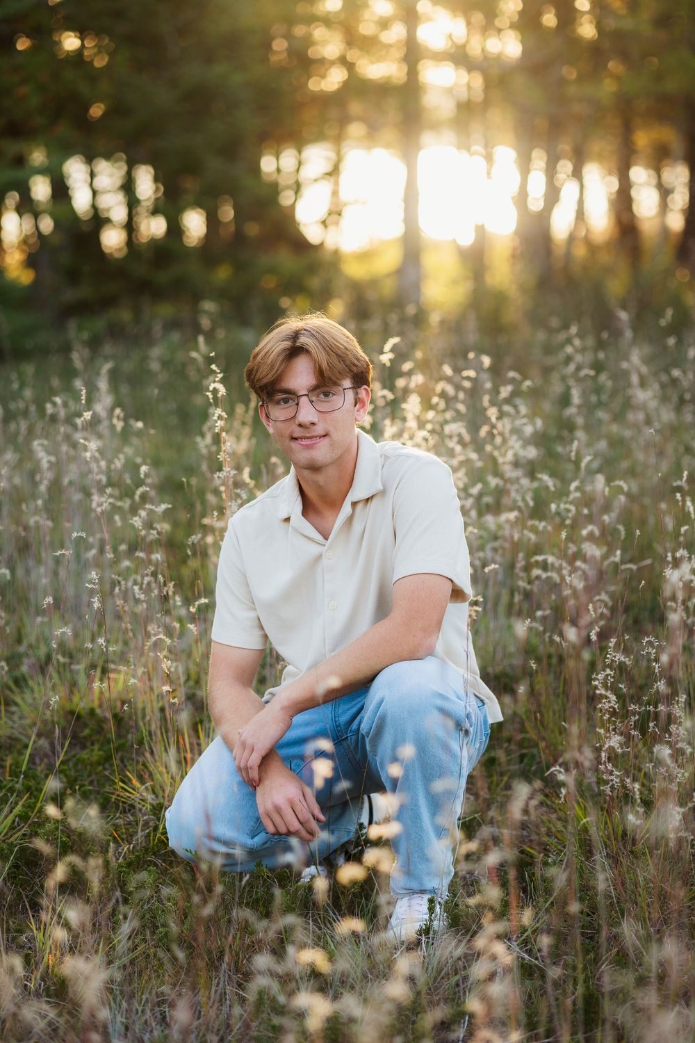 Casual portrait in a wildflower meadow at golden hour with sunlit trees in background.