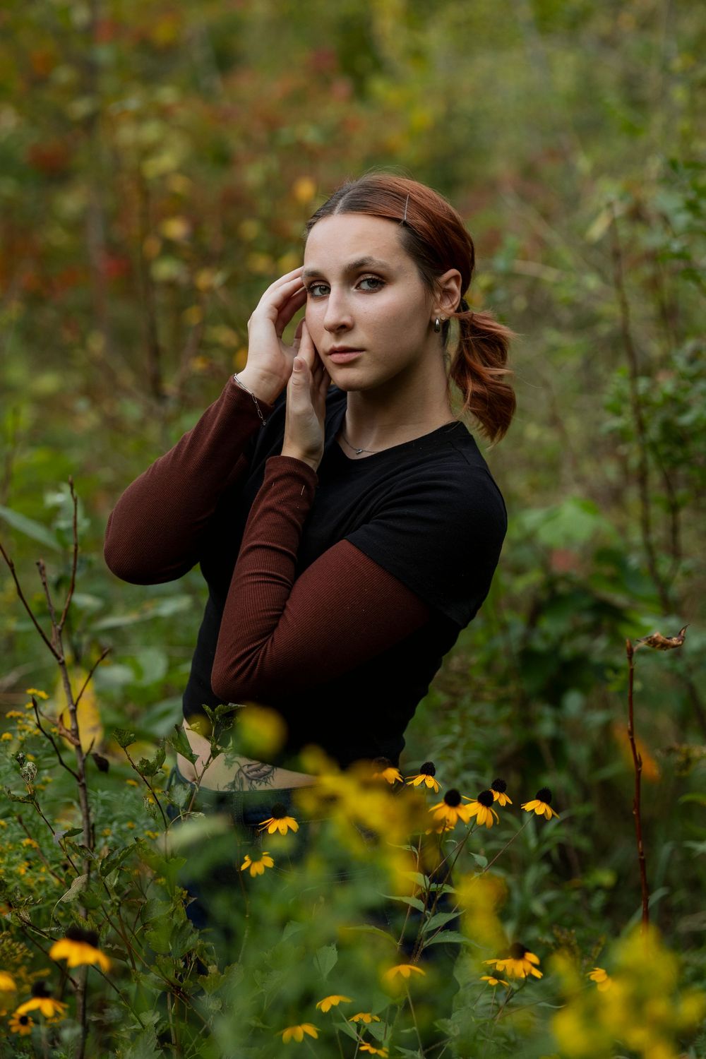 Artistic portrait in a garden with yellow wildflowers and burgundy long sleeves.