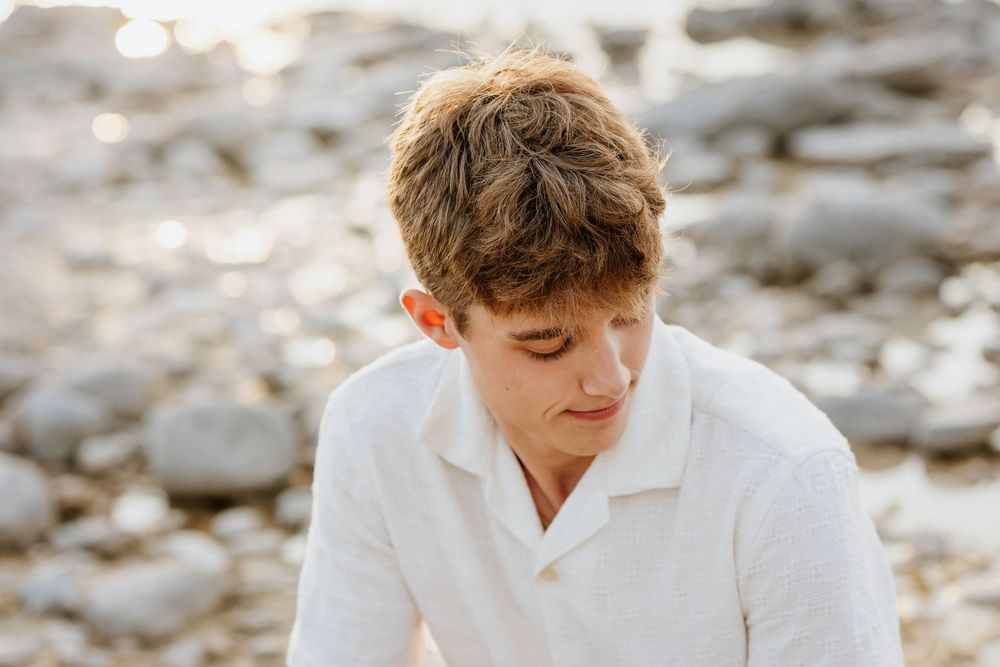 Candid seaside portrait in white shirt with sunlit rocks in background.
