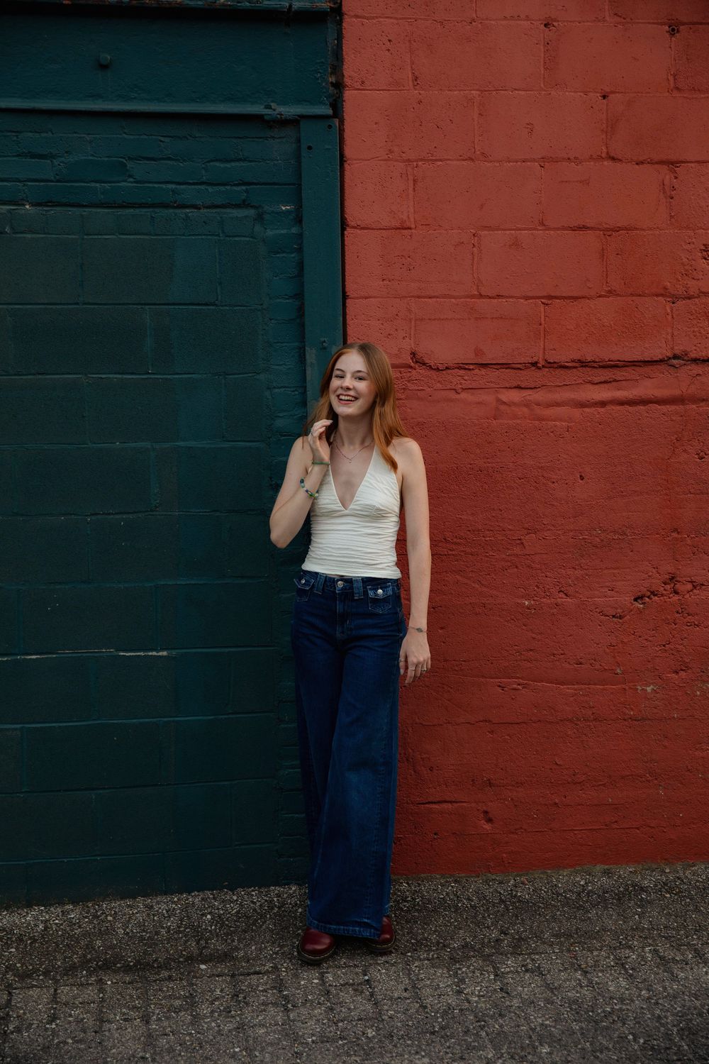 A casual portrait against vibrant red and teal painted brick walls.