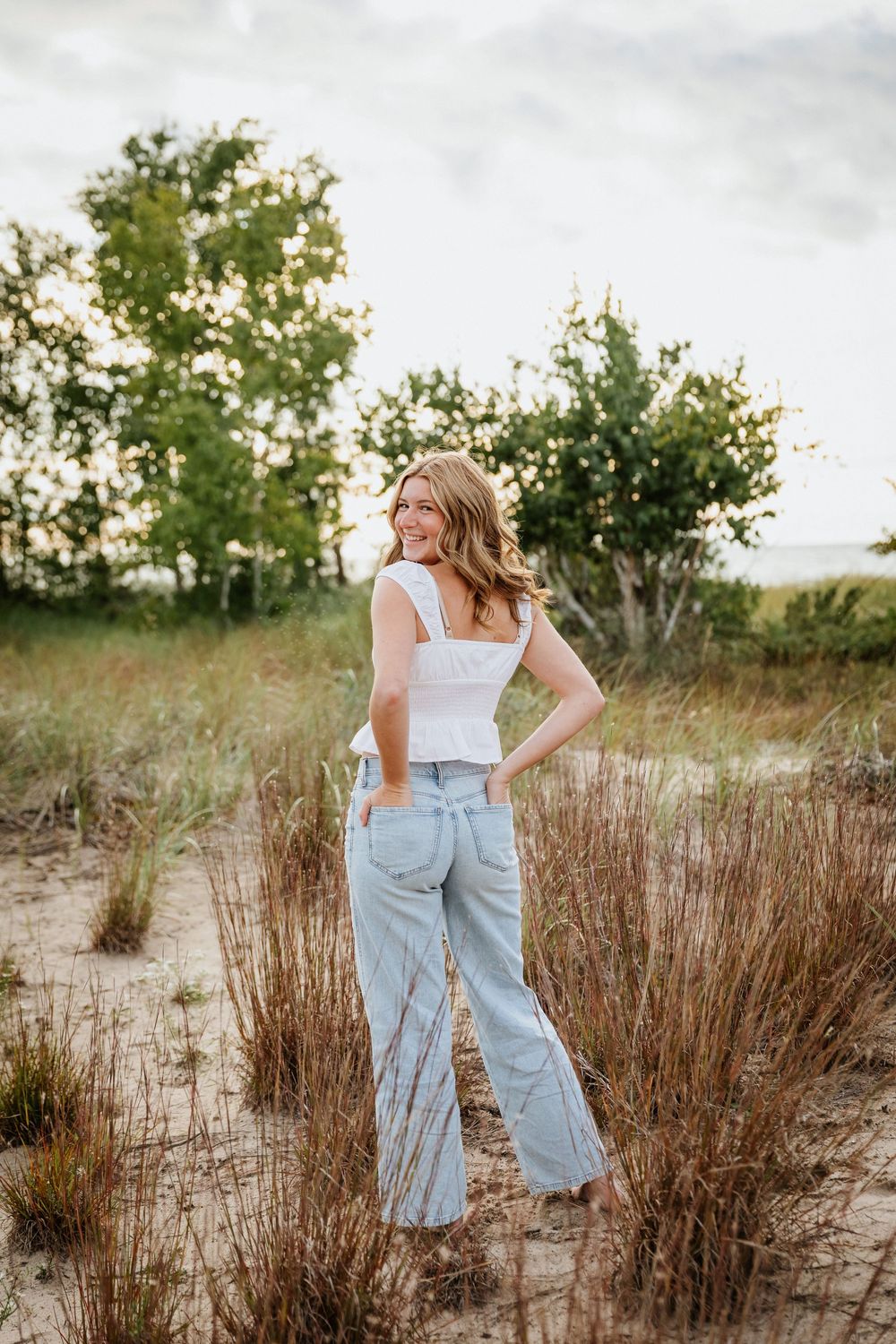 Person poses in casual summer outfit among beach grass during sunset.