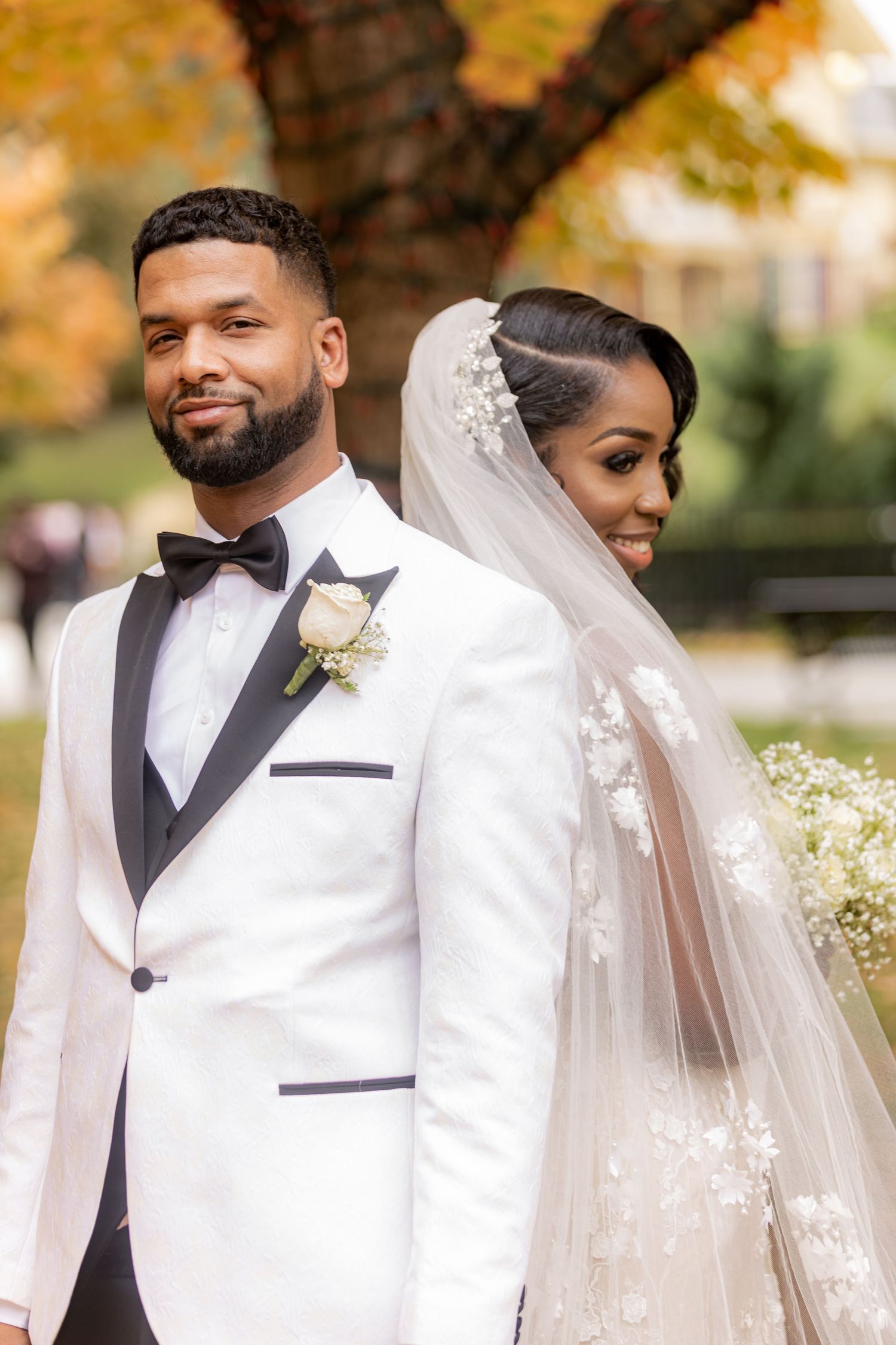 Bride and groom pose back-to-back outdoors in autumn, she wears floral veil, he wears white tuxedo. Wedding Taken by BEXPRO in Brampton, ON