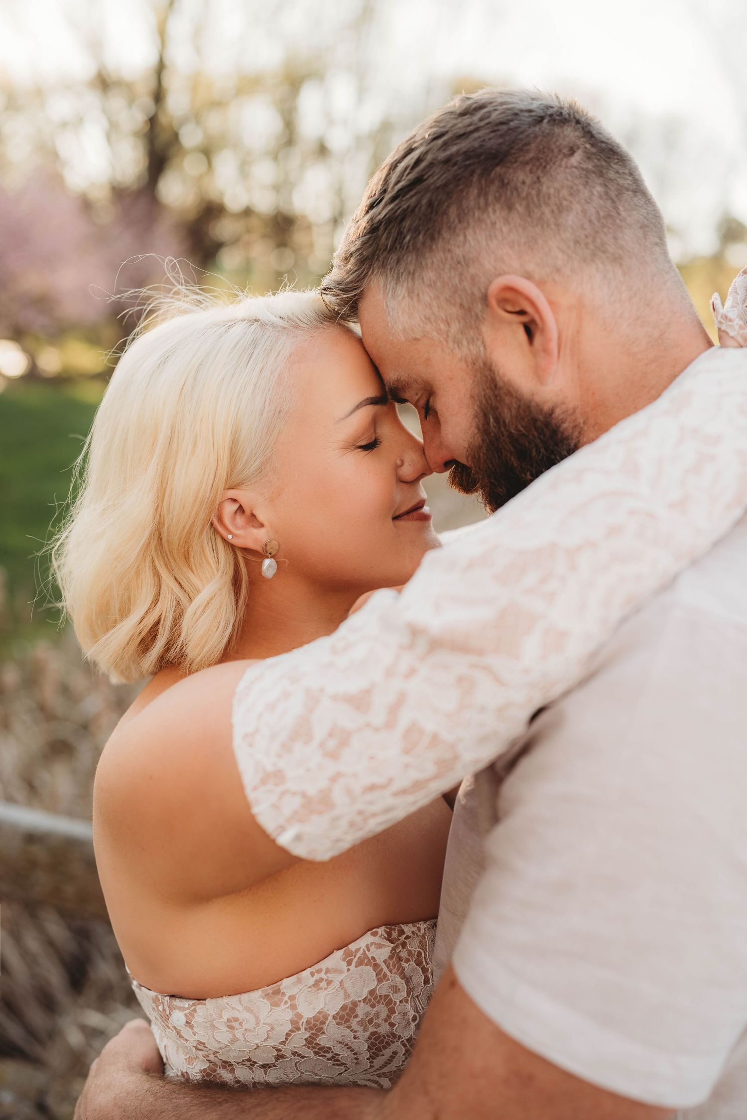 Romantic couple embracing closely with foreheads touching outdoors in warm golden light.