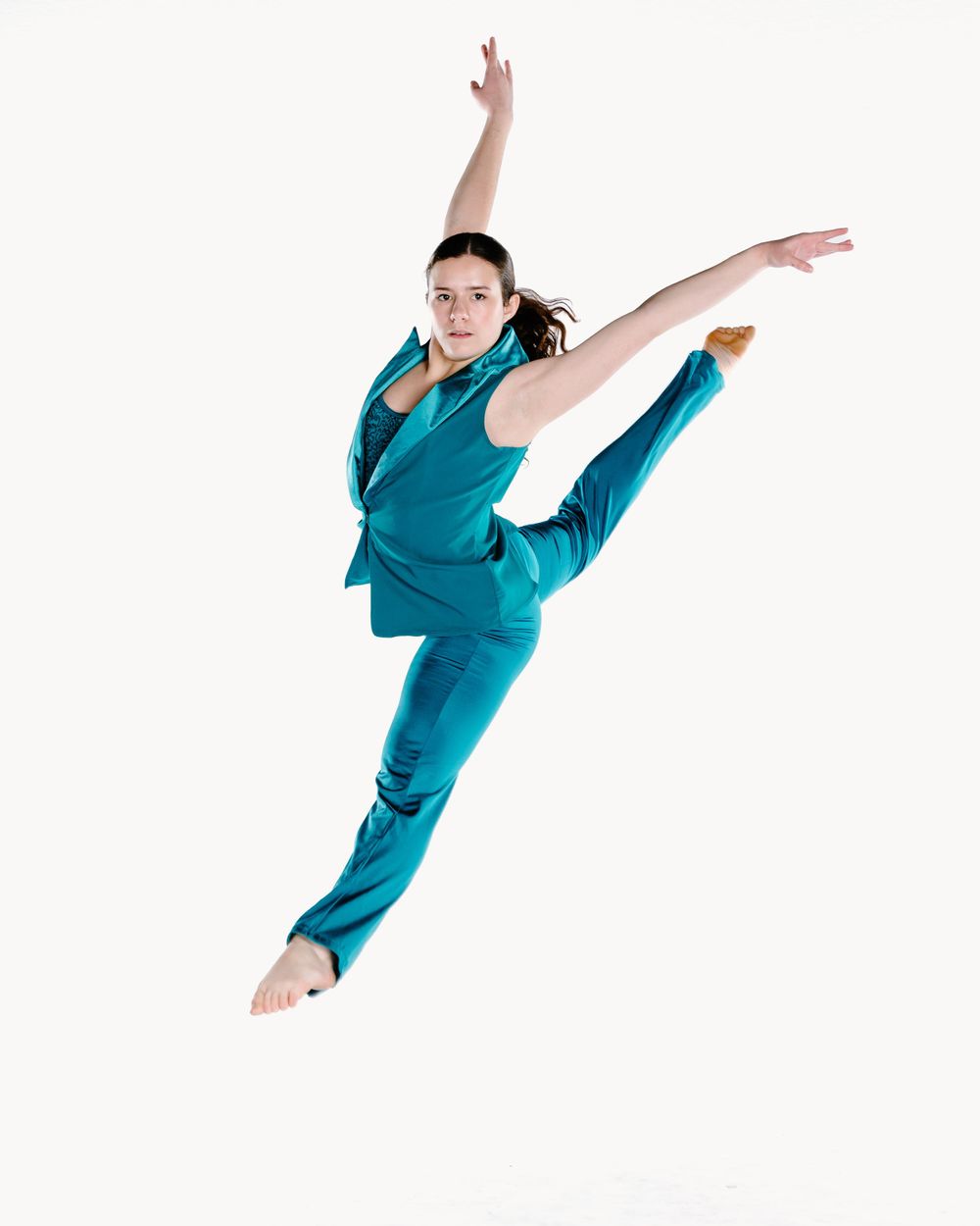 Dancer in bright teal suit performs an elegant split leap against white background.