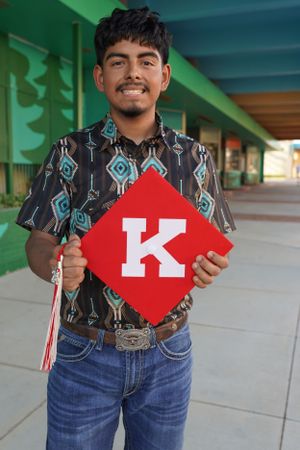 man posing smiling with graduation cap with K on it
