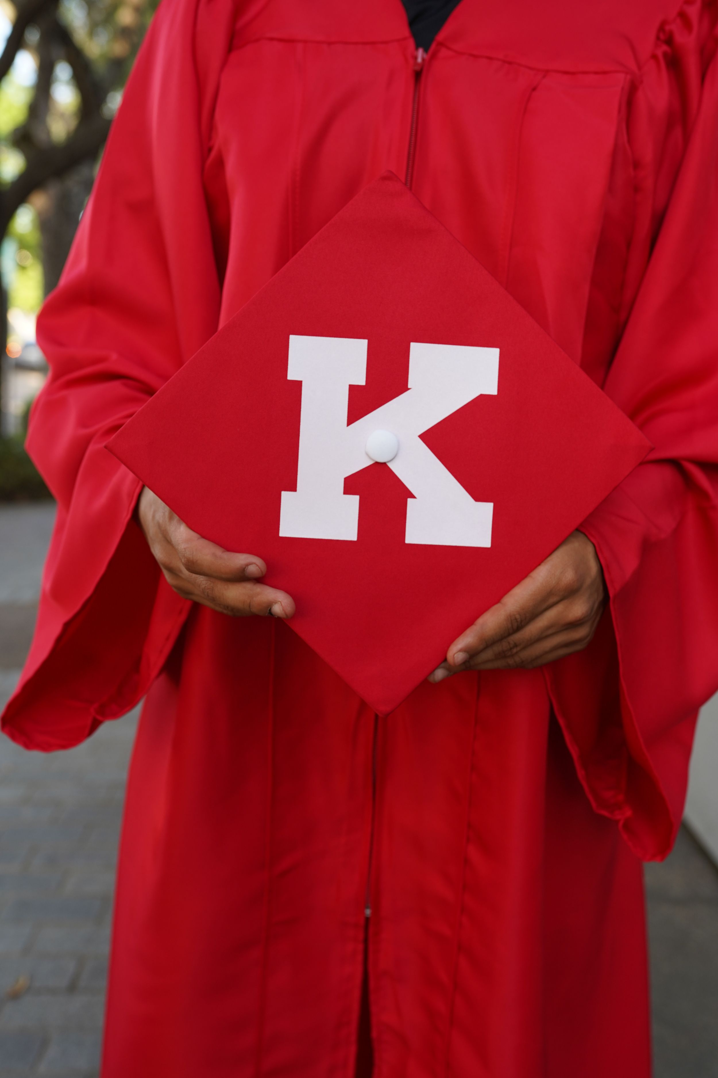 man holding graduation cap with K on it