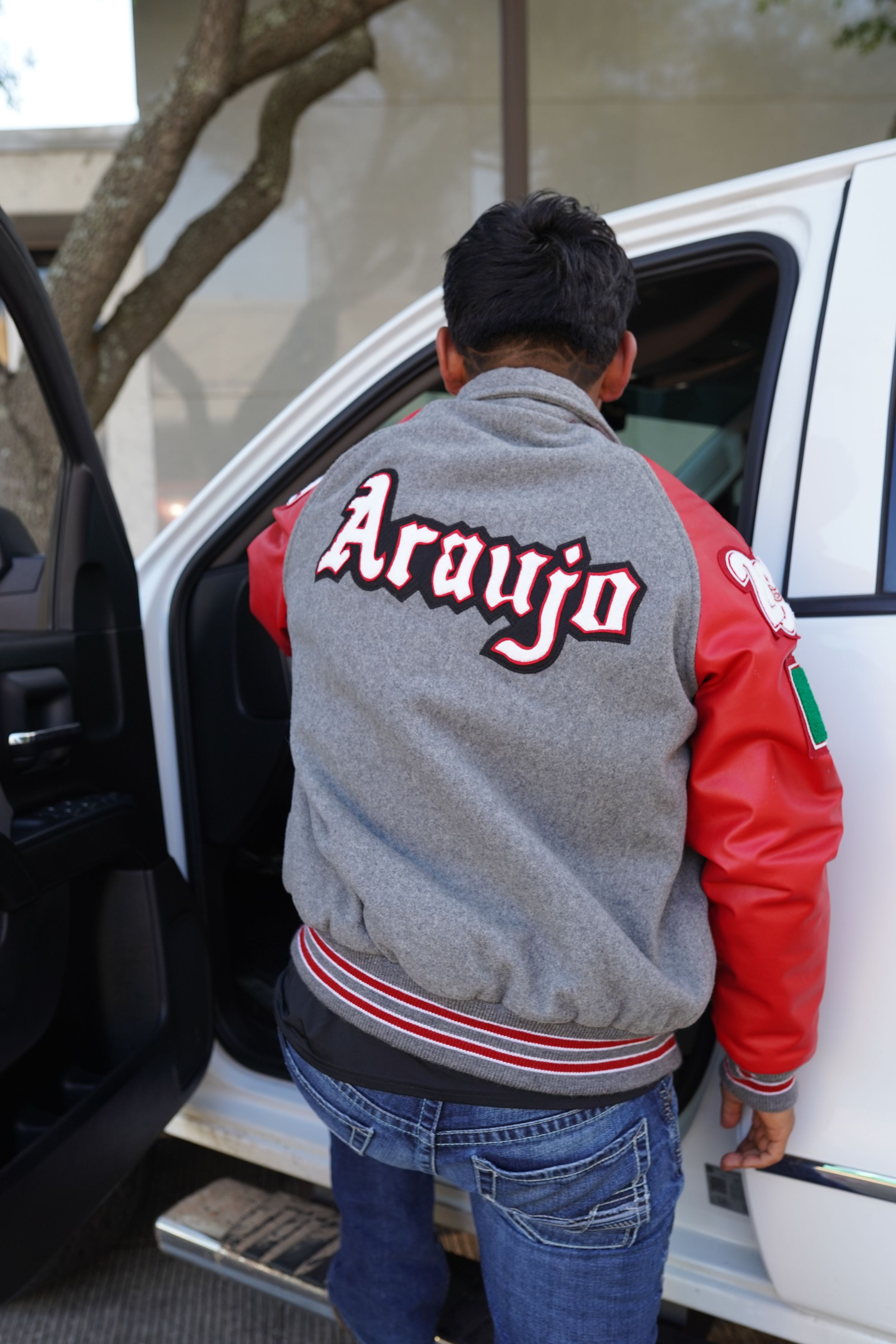 man stepping into truck with "araujo" written on back of letterman jacket