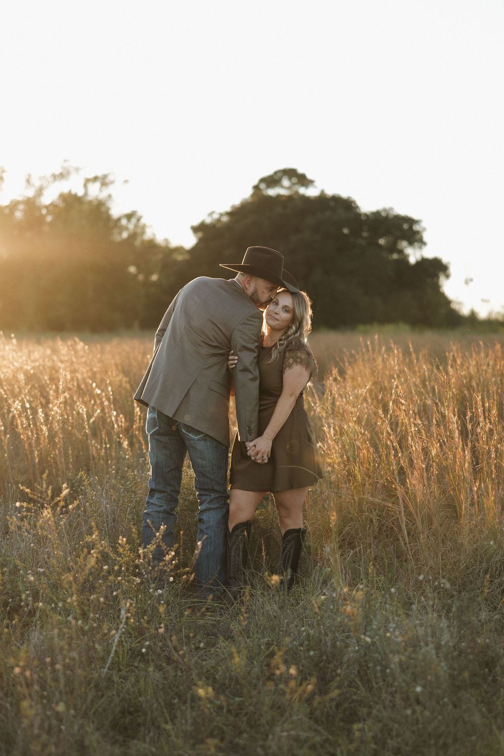A couple shares an intimate moment in a golden wheat field at sunset, creating a romantic silhouette against nature.