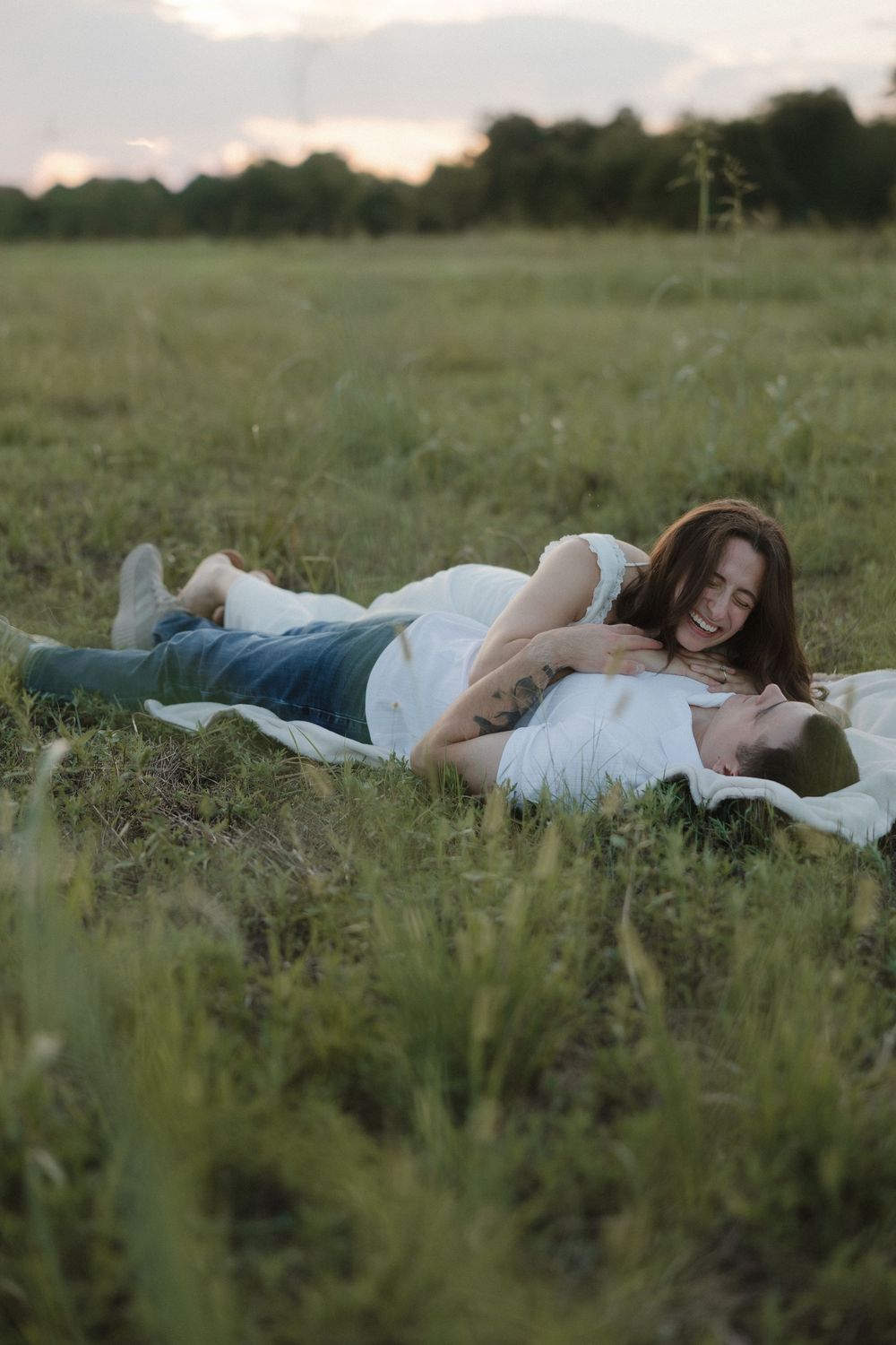 A couple lying together in a peaceful meadow during sunset surrounded by tall grass and wildflowers.