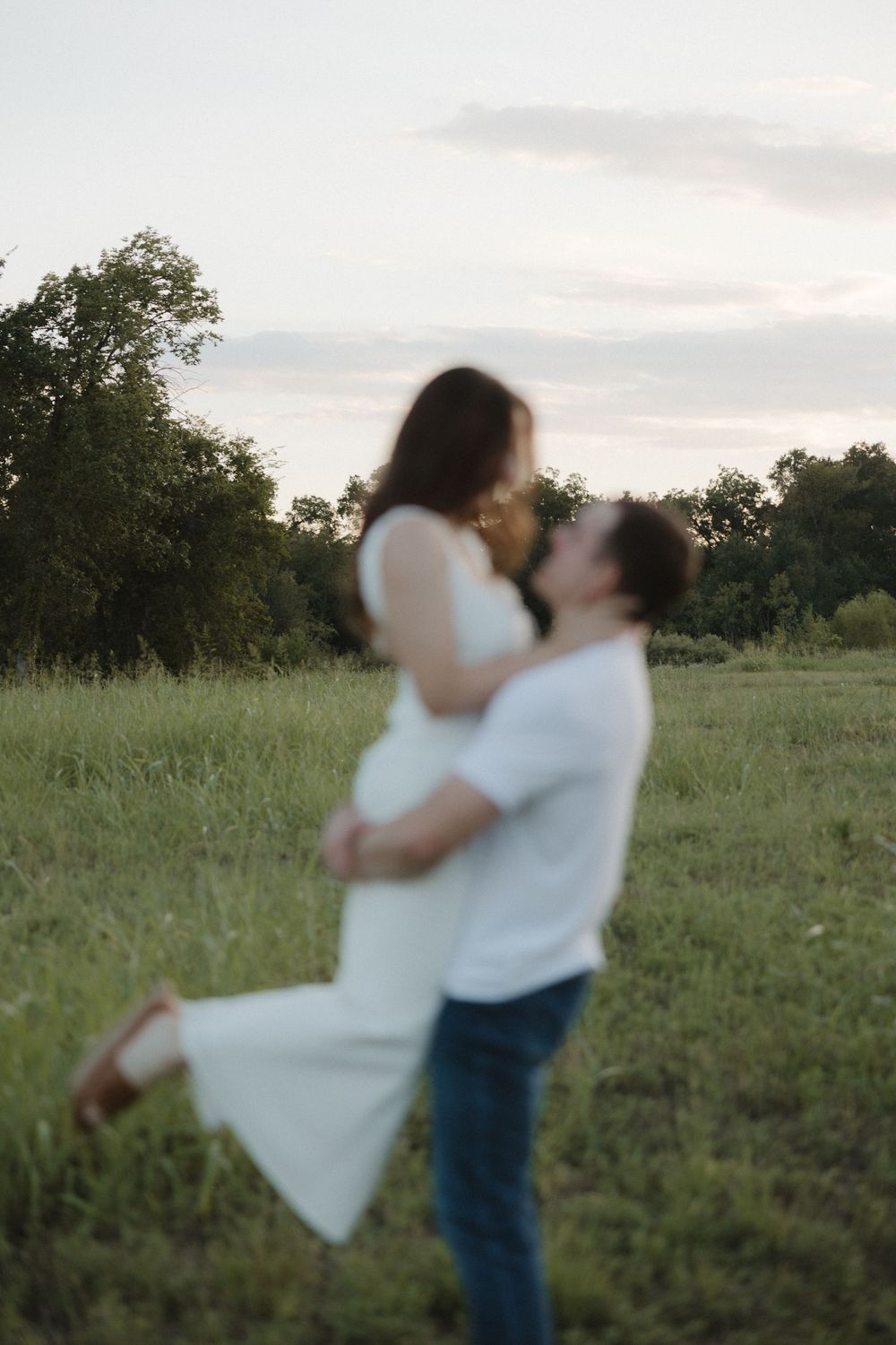 A couple dancing and twirling joyfully together in a green summer field at dusk.