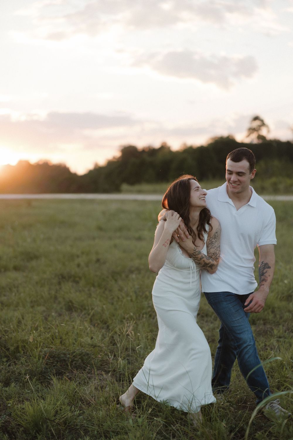 A couple shares romantic moments in a grassy field during golden hour sunset.
