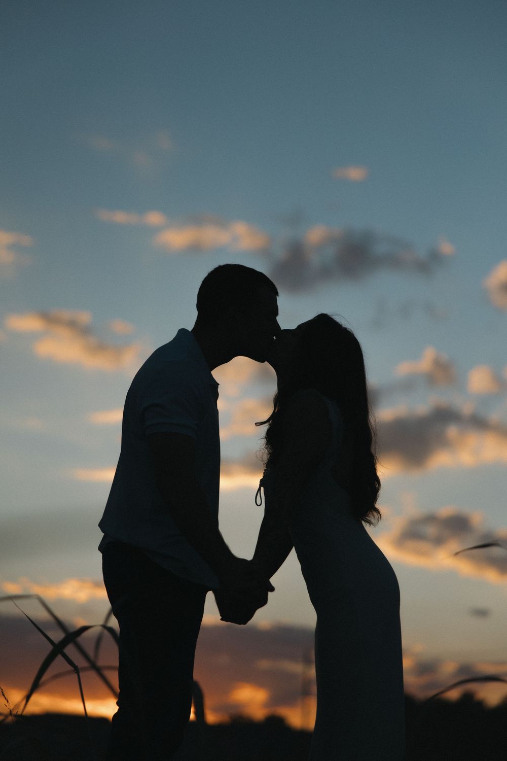 Silhouettes of two figures against a dramatic sunset sky with wispy clouds.