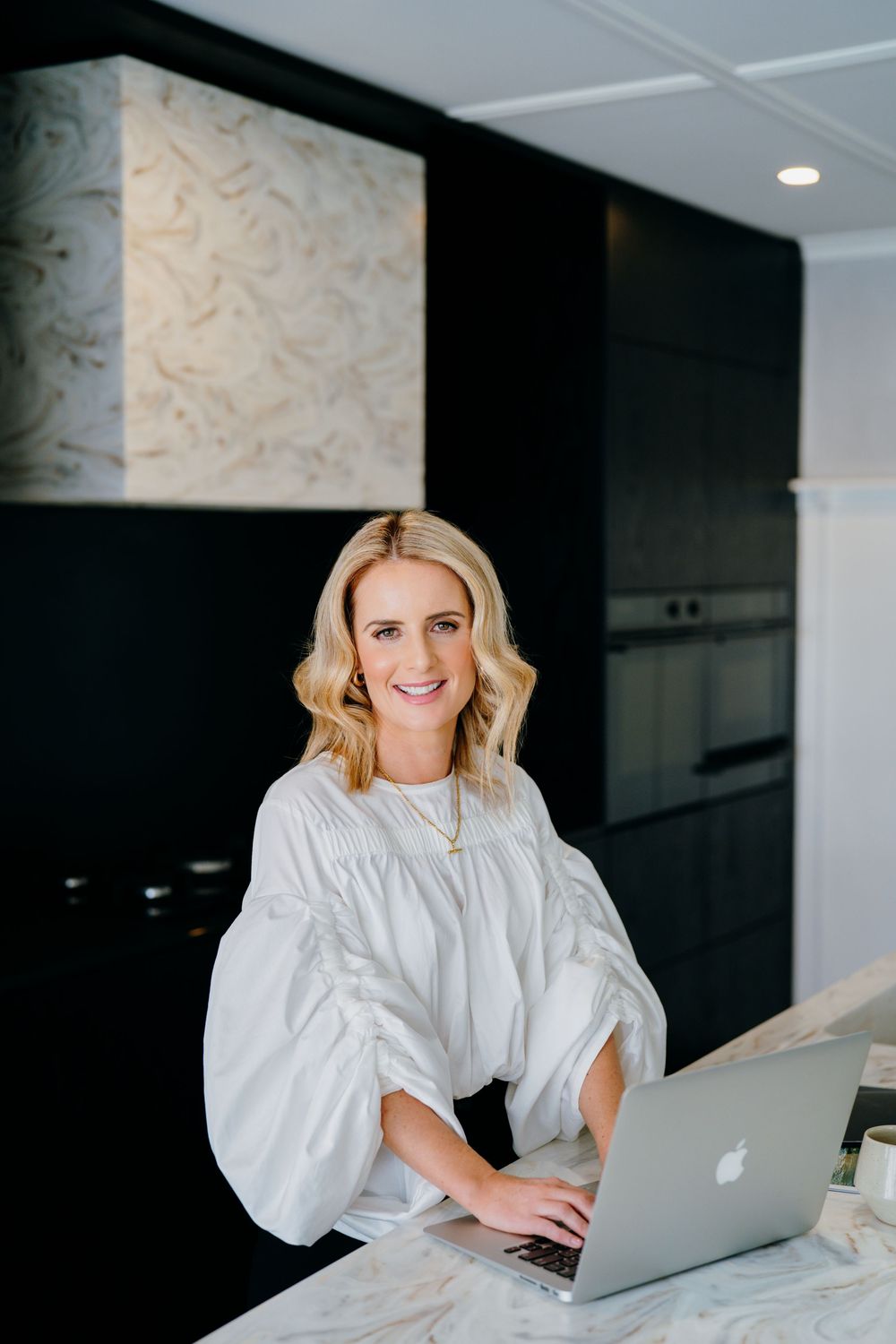 Professional working at a modern desk with laptop in bright office space wearing white blouse.