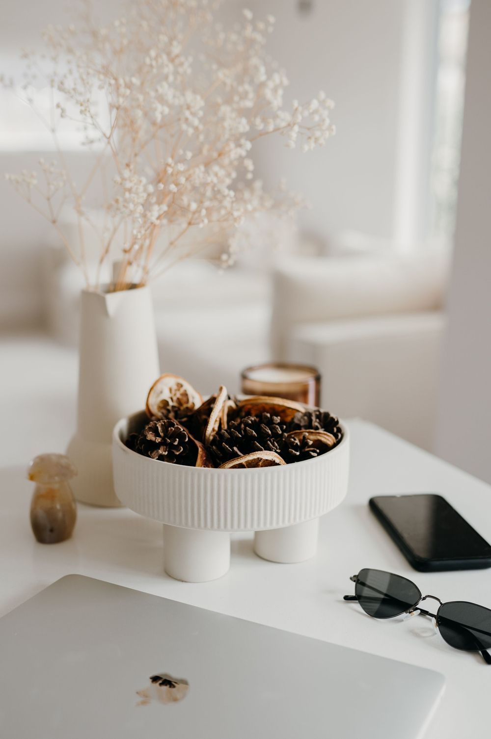 A minimalist white windowsill decorated with delicate dried flowers in small ceramic pots and sunglasses.