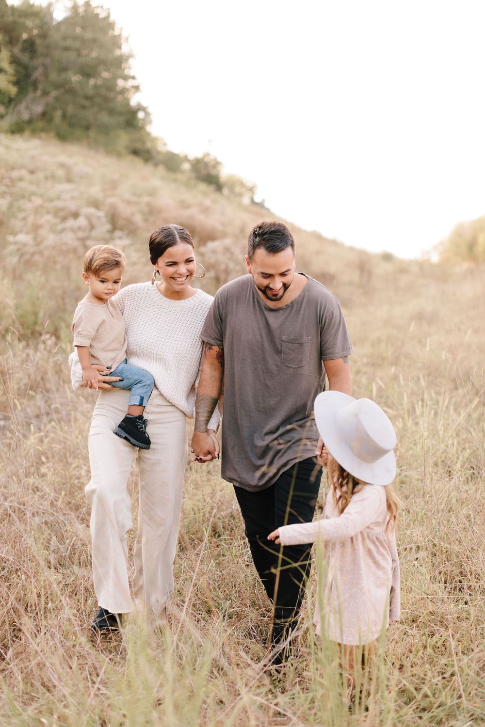 Family walking together through a golden grass field on a sunny hillside enjoying an outdoor afternoon.