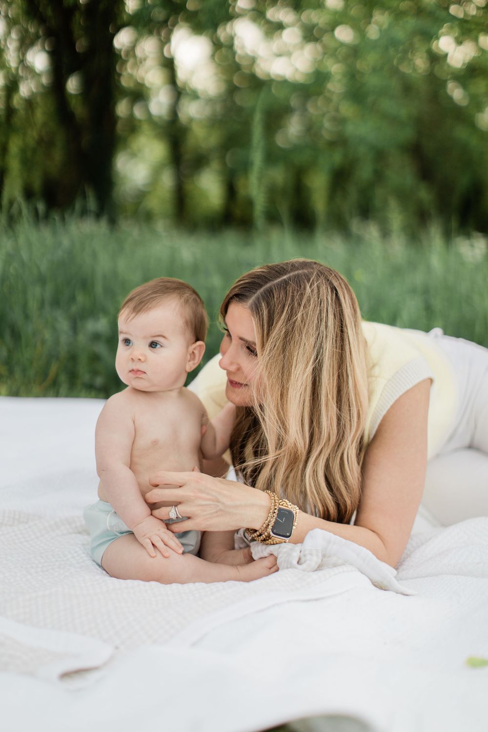 A tender moment captured on a white blanket outdoors as parent and baby share intimate bonding time in nature.