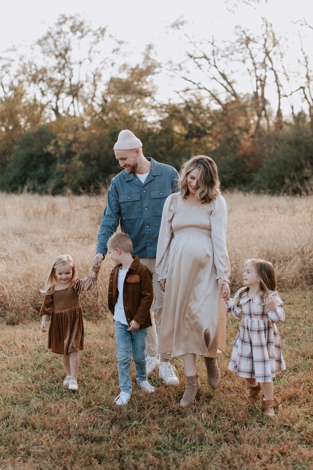 A family enjoys an autumn walk together in a field with golden grass and bare trees in the background.