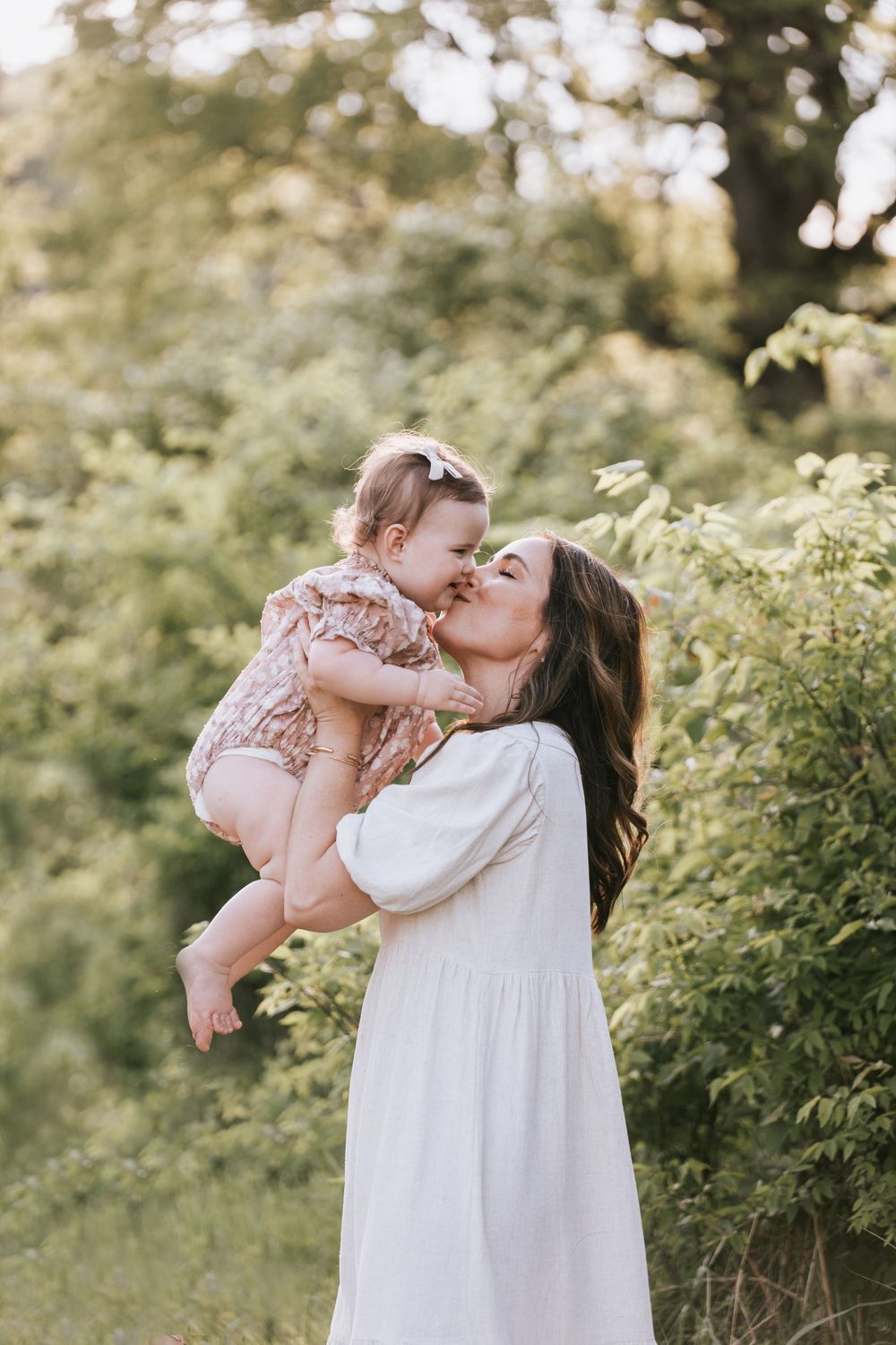 A tender moment captured in an outdoor setting with soft natural lighting and green foliage in the background.