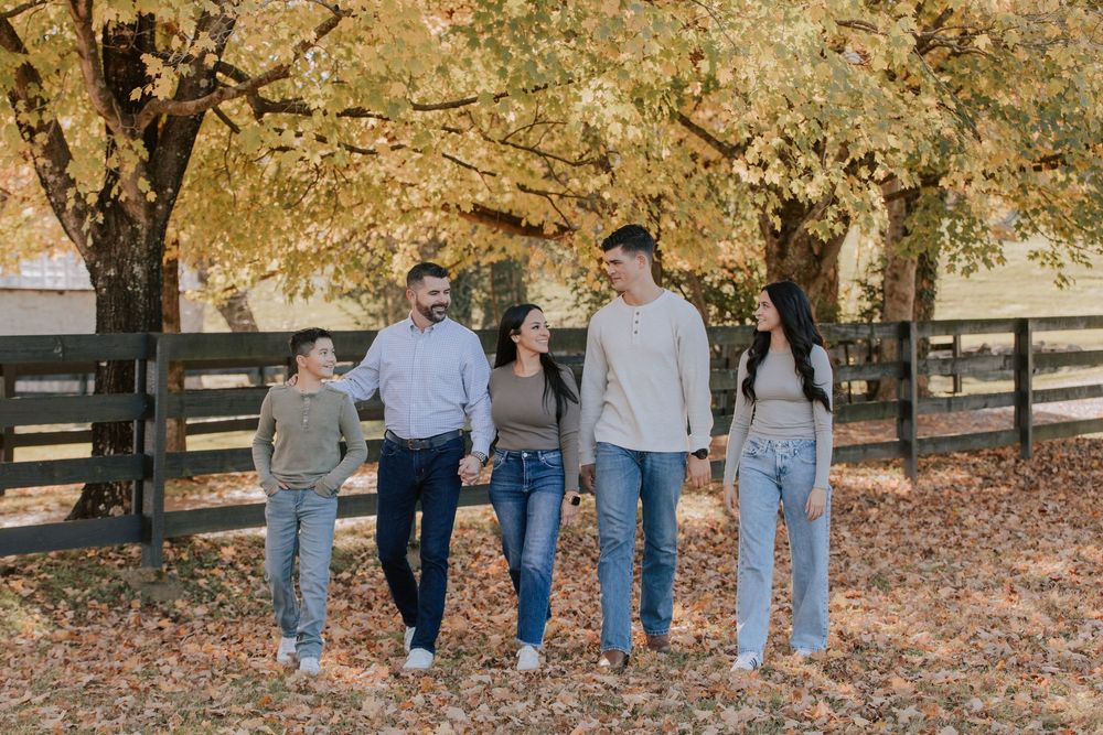 Group walks together through a fall landscape with colorful autumn leaves scattered on the ground beneath large trees.