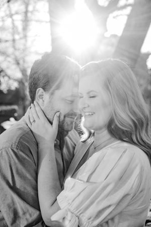 Black and white portrait of tender moment with sunlight streaming through trees.