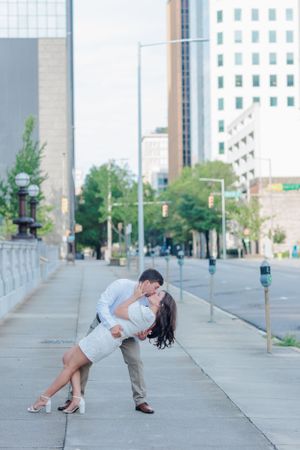 Romantic dance dip pose on city sidewalk with urban landscape backdrop.