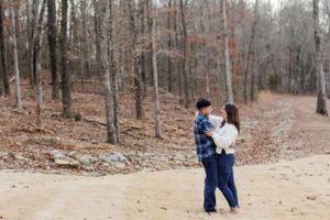 Couple embraces on autumn forest trail during engagement session.