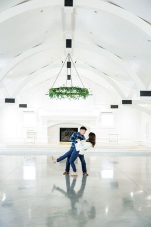 Dancing couple in white chapel venue with greenery chandelier and vaulted ceiling.